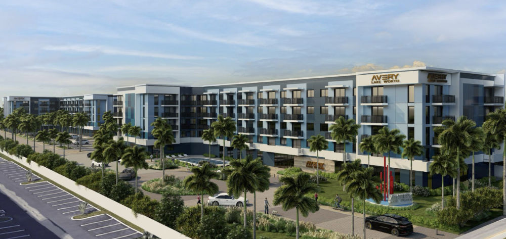 Modern hotel exterior with multiple floors, featuring blue and white color schemes. Surrounding palm trees and landscaped grounds. A parking area is visible in the foreground.